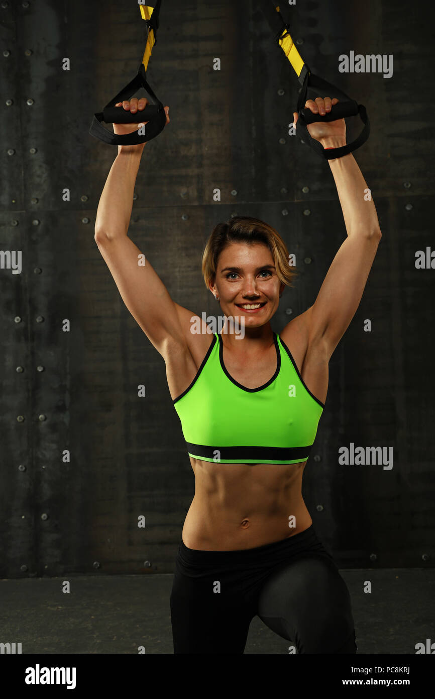 Una giovane donna di atletica a crossfit training, esercitando con trx sospensione cinghie di fitness su sfondo scuro, vista frontale, guardando la fotocamera Foto Stock