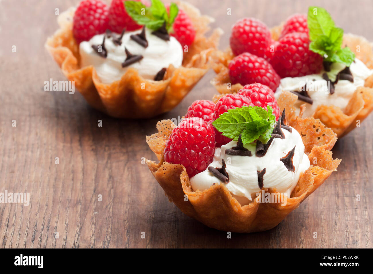 Il Brandy snap cesti con gelato e frutti di bosco su un tavolo di legno Foto Stock
