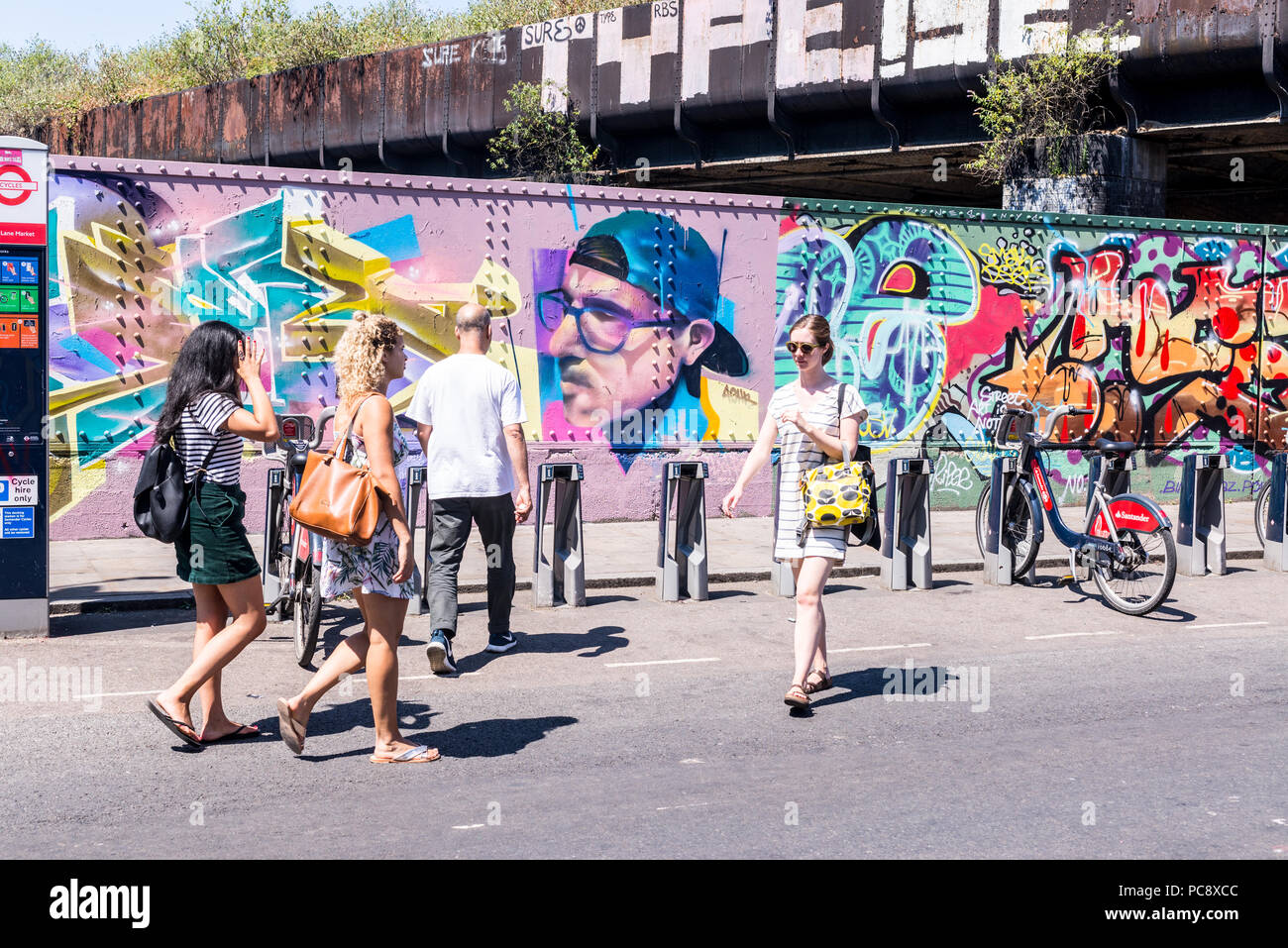 Street View di Brick Lane con giovani hipsters e turisti a piedi. Street Art graffiti murali in background. Brick Lane, Shoreditch, London, Regno Unito Foto Stock