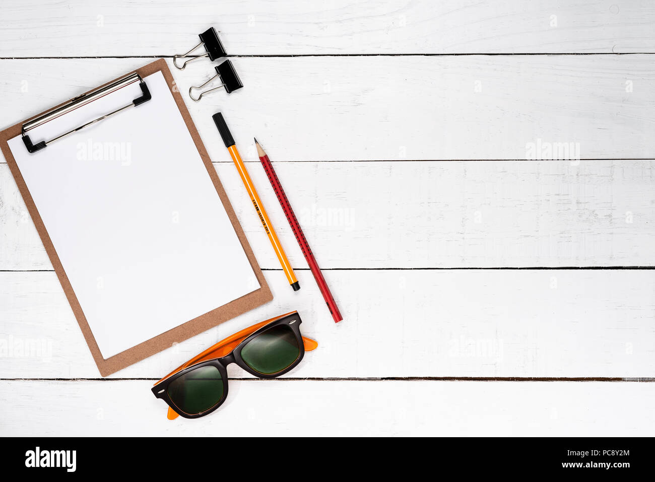 White notepad con penna gialla, fermagli per carta, matita rossa e occhiali scuri su bianco sullo sfondo di legno Foto Stock