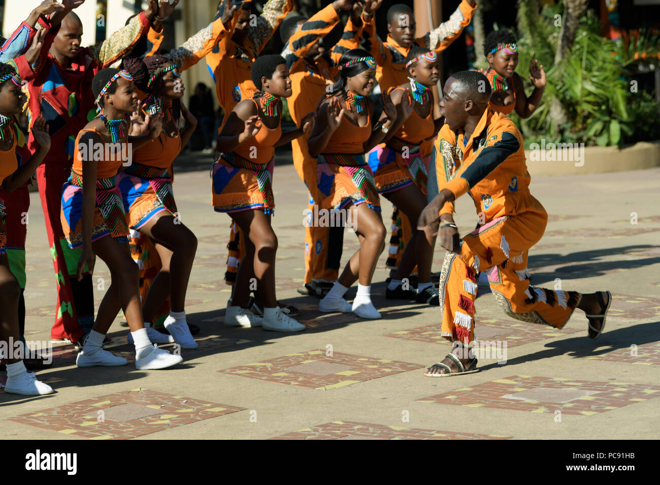 I giovani adulti maschi e femmine di canzoni e balli di gruppo risponde alle direzioni di troupe leader all'Ushaka Marine World, Durban Foto Stock