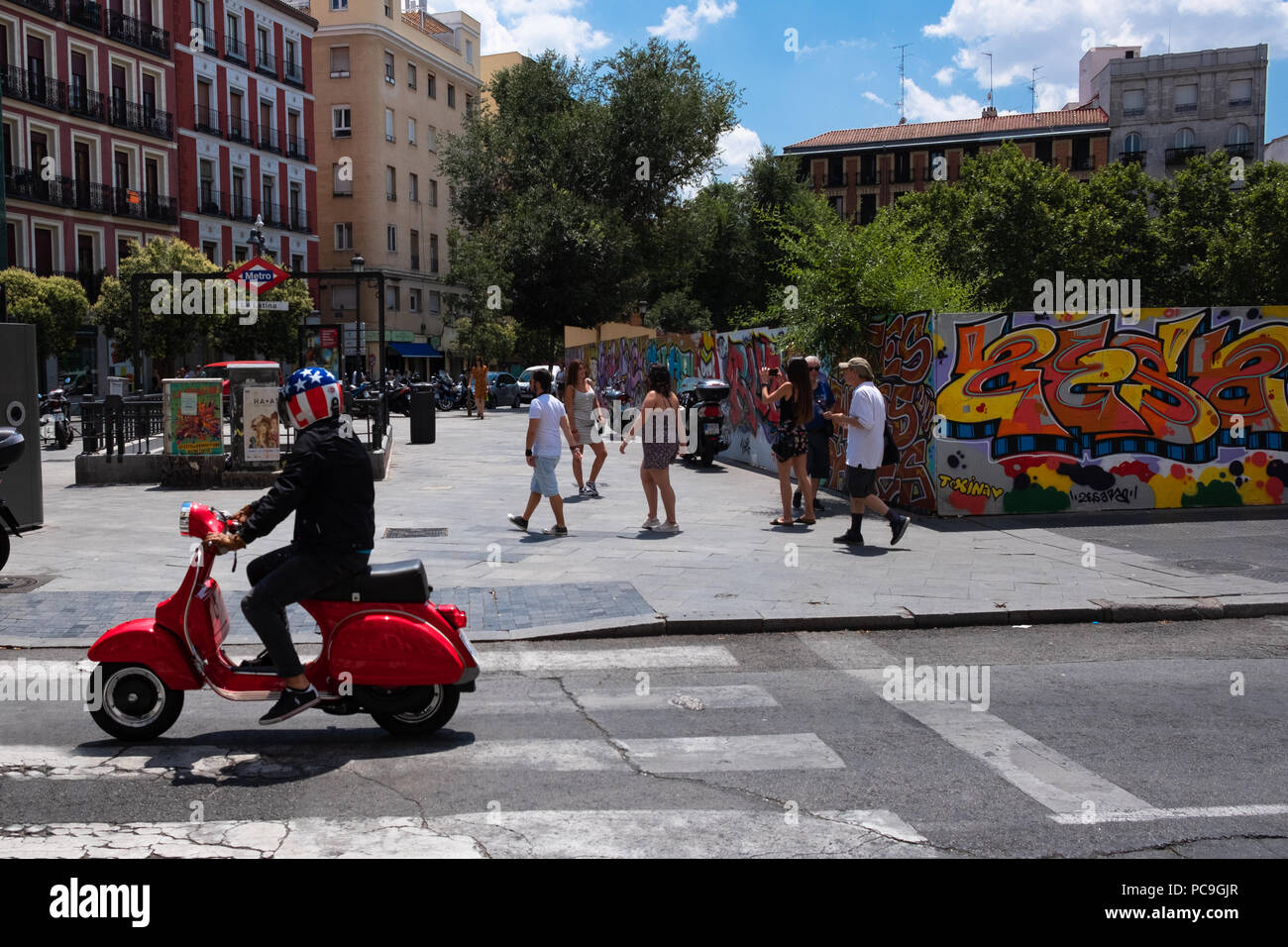 Red vintage scooter lookalike rigidi mediante una delle strade di Madrid in una giornata di sole, pilota indossa un casco con la bandiera degli Stati Uniti di colori e design. Foto Stock