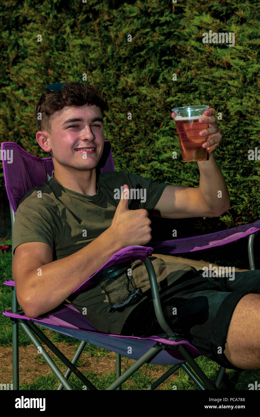 Giovane adulto seduto fuori godendo il sole estivo con una birra in un giardino Foto Stock