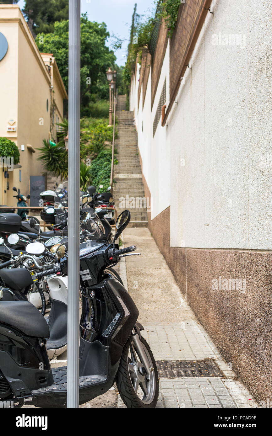 Mazzetto di scooter parcheggiato in strada molto stretta con scale di Barcellona. Foto Stock