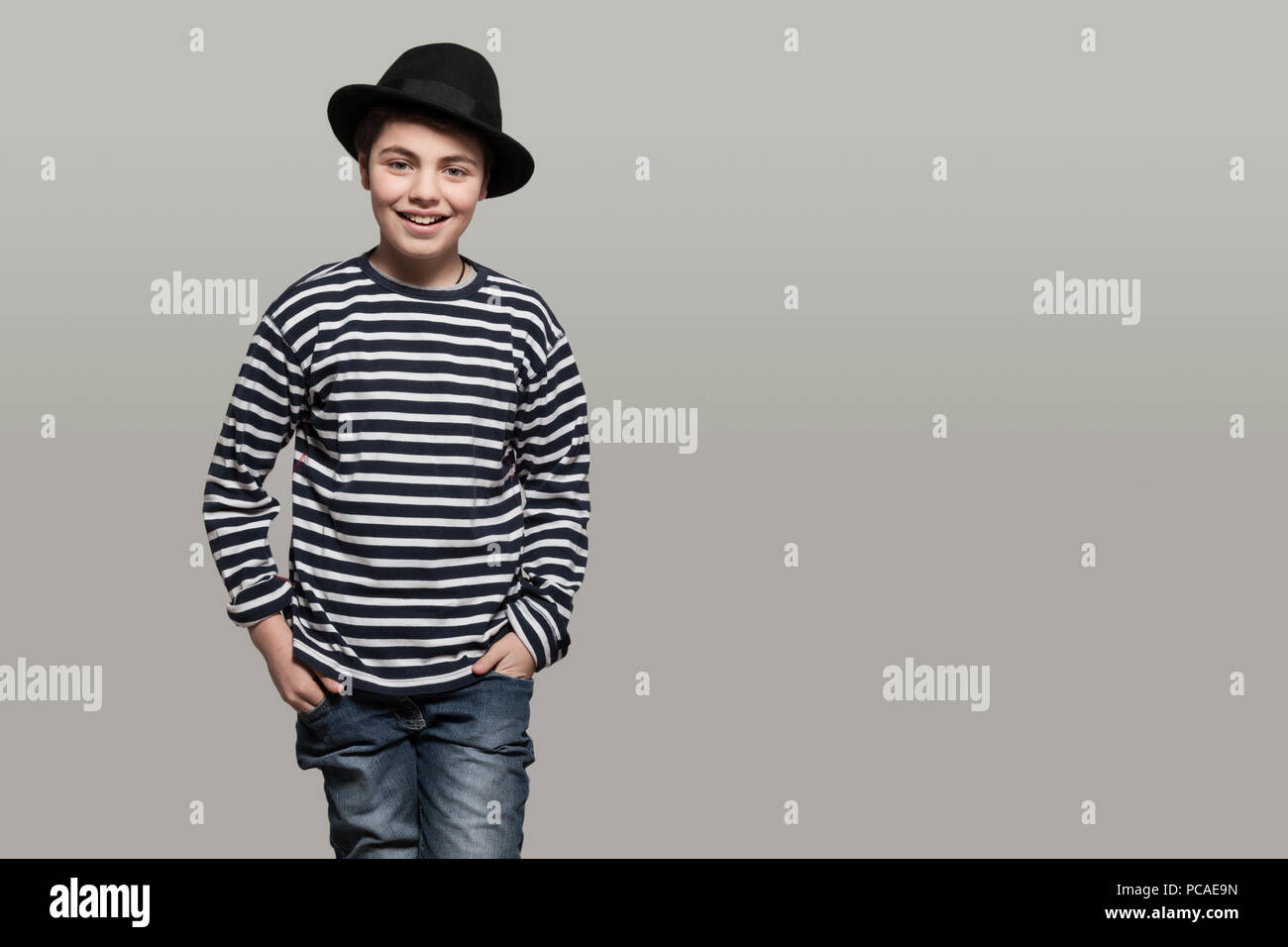 Sorridente ragazzo indossa una camicia a righe e cappello nero, le mani in tasca Foto Stock