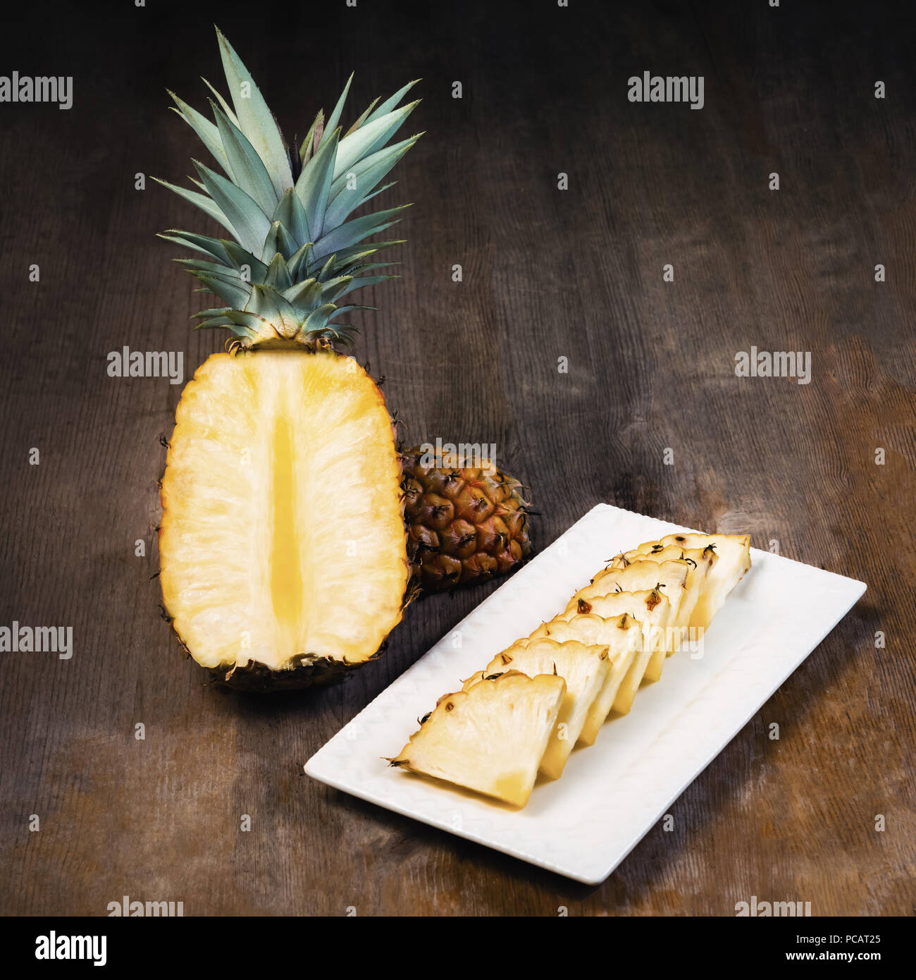 Ananas frutta tagliata a metà trimestre, e cunei e visualizzati su piastra in bianco e lo sfondo di legno. Composizione quadrata. Succosa coltivati biologicamente mature e Foto Stock
