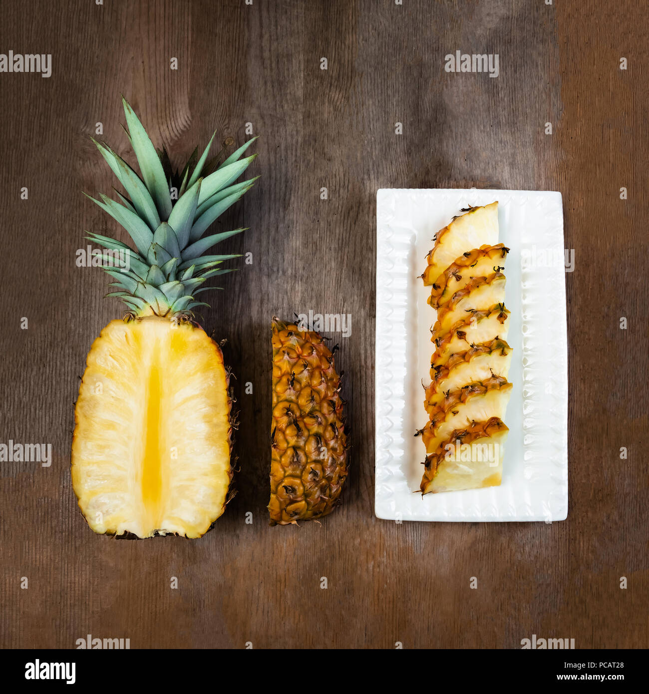 Ananas frutta tagliata a metà trimestre, e cunei e visualizzati su piastra in bianco e lo sfondo di legno. Composizione quadrata. Succosa coltivati biologicamente mature e Foto Stock