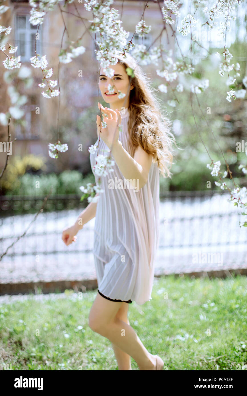 Bellissima fanciulla si erge tra gli alberi in fiore. Fiori bianchi. La molla la ragazza con i capelli in un abito di colore beige. Ritratto. Romanticismo Foto Stock