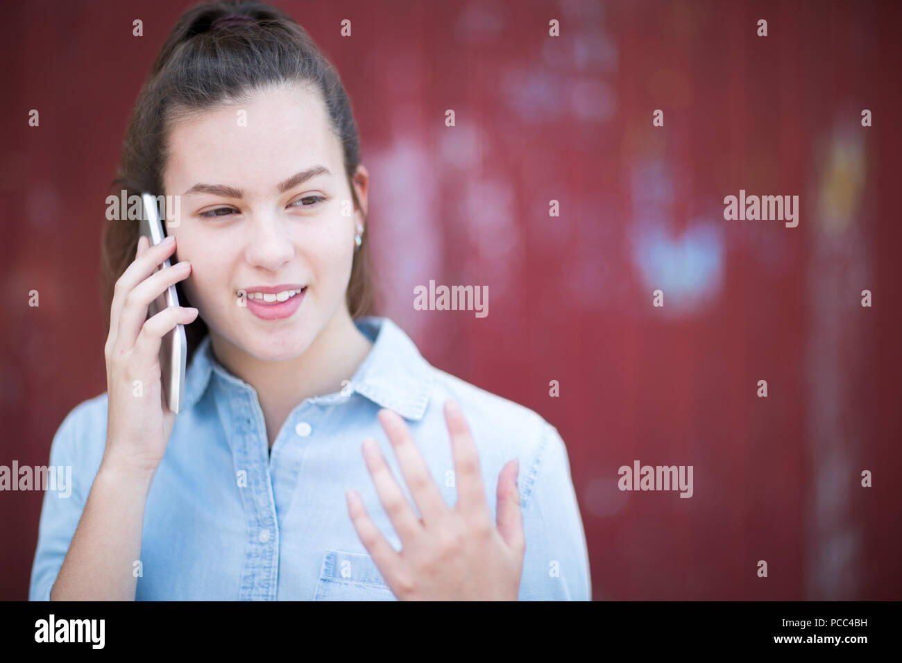 Ragazza adolescente parlando al di fuori sul telefono cellulare in contesto urbano Foto Stock