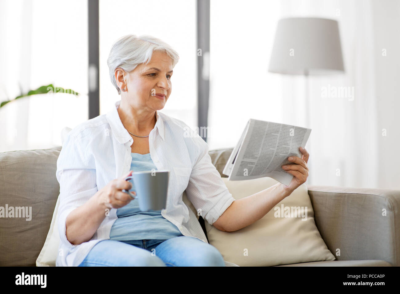 Senior donna con caffè quotidiano di lettura a casa Foto Stock