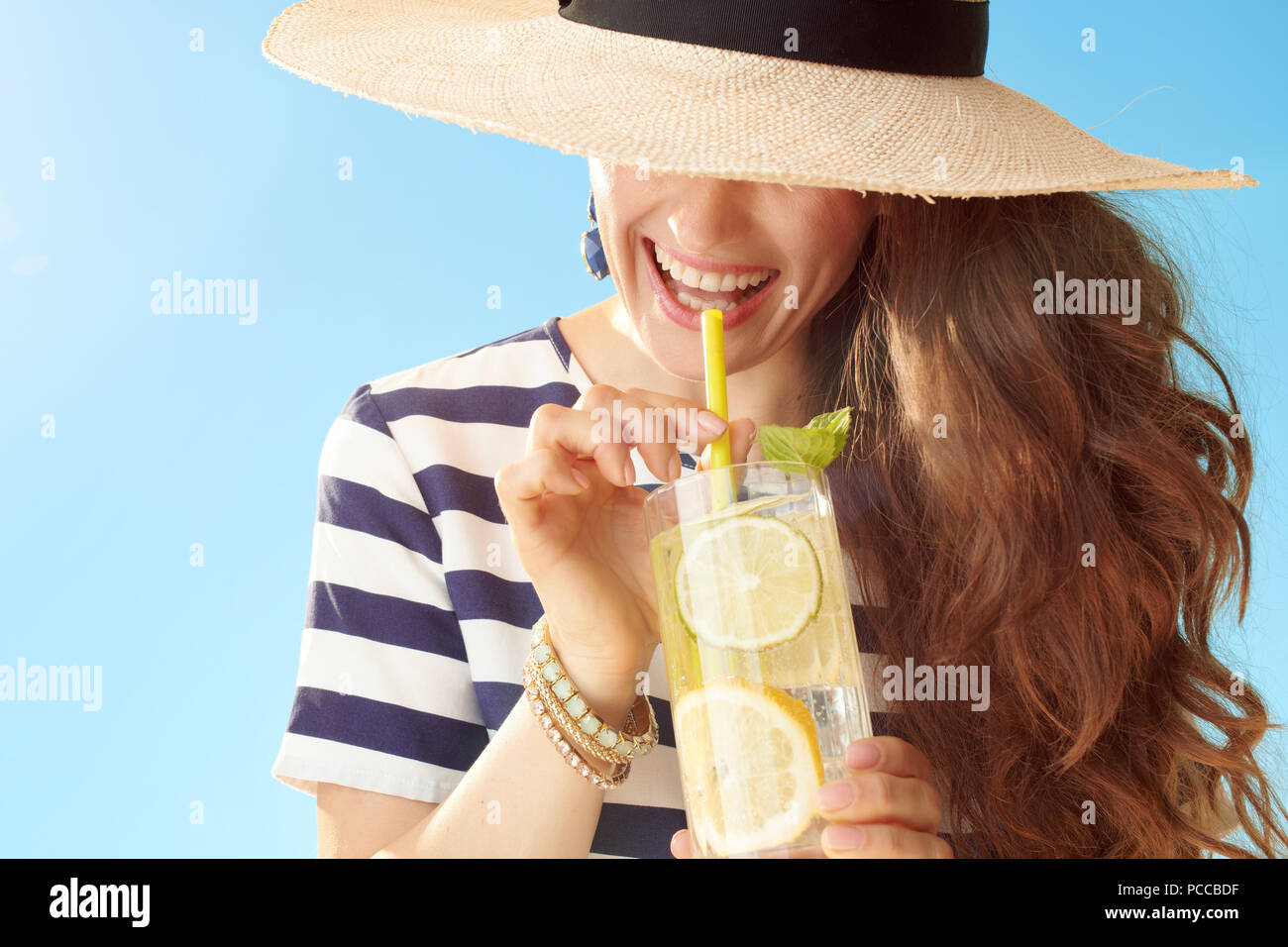 Moda donna nel cappello di paglia contro il cielo blu di bere un cocktail rinfrescante Foto Stock