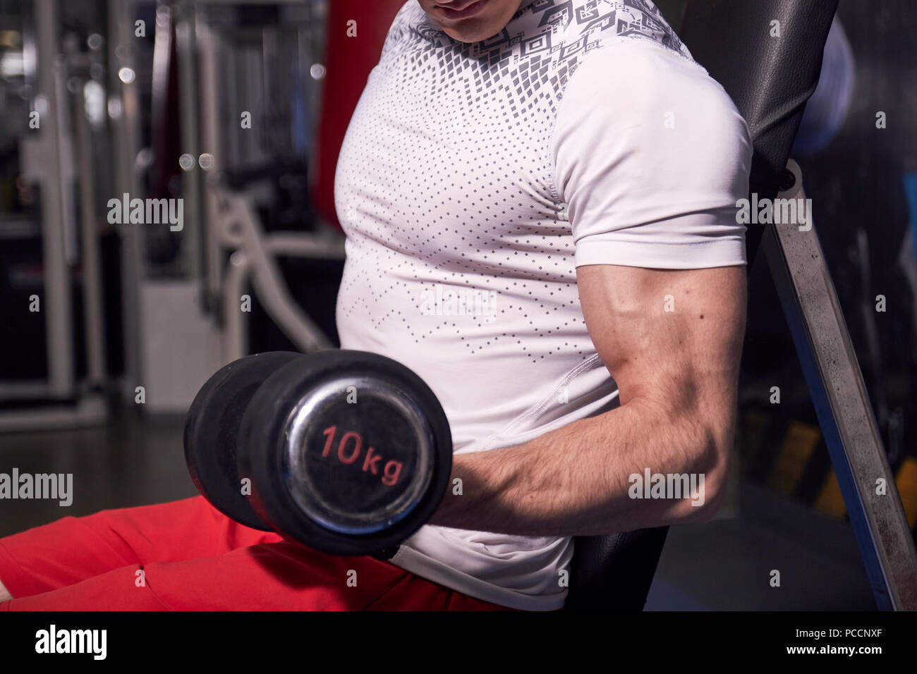 Close up di forte braccio muscoloso bicipite, tenendo il manubrio. Un giovane uomo che indossa abbigliamento sportivo, camicia pantaloncini. Foto Stock