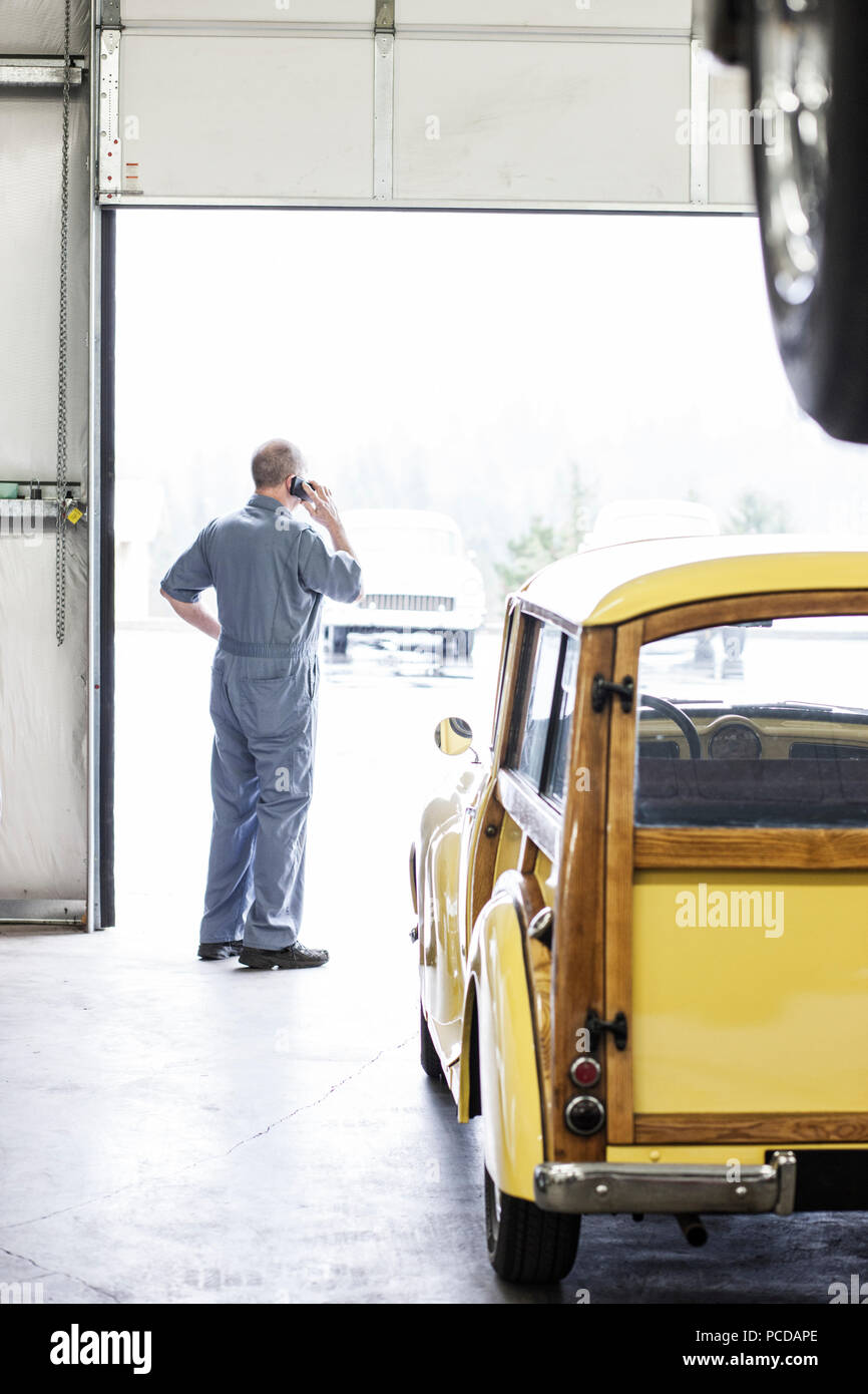 Vista da dietro di un proprietario di una riparazione auto shop sul suo telefono cellulare. Foto Stock