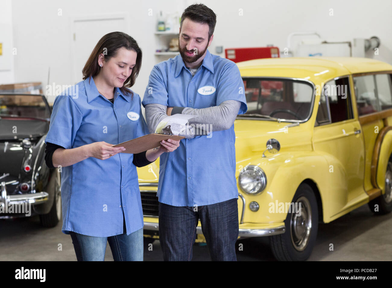 Una coppia di soggetti di razza caucasica maschio e femmina meccanica auto a parlare nel corso di una riparazione scivolare in un auto classica officina di riparazione. Foto Stock