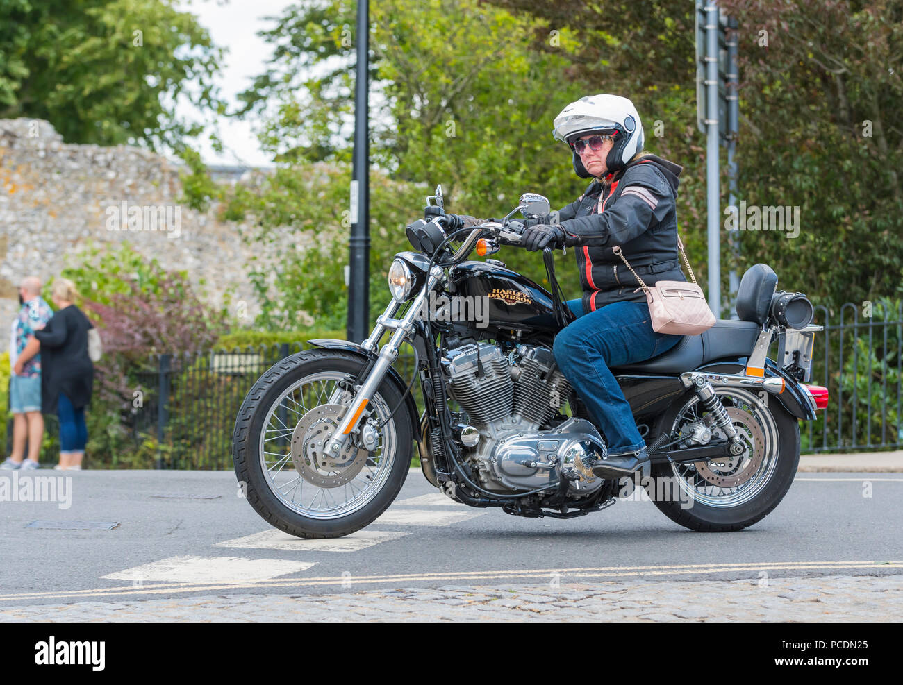 Donna che cavalca una motocicletta Harley Davidson Bike 883 Sportster con borsa sopra le spalle nel Regno Unito. Motociclista femminile. Foto Stock