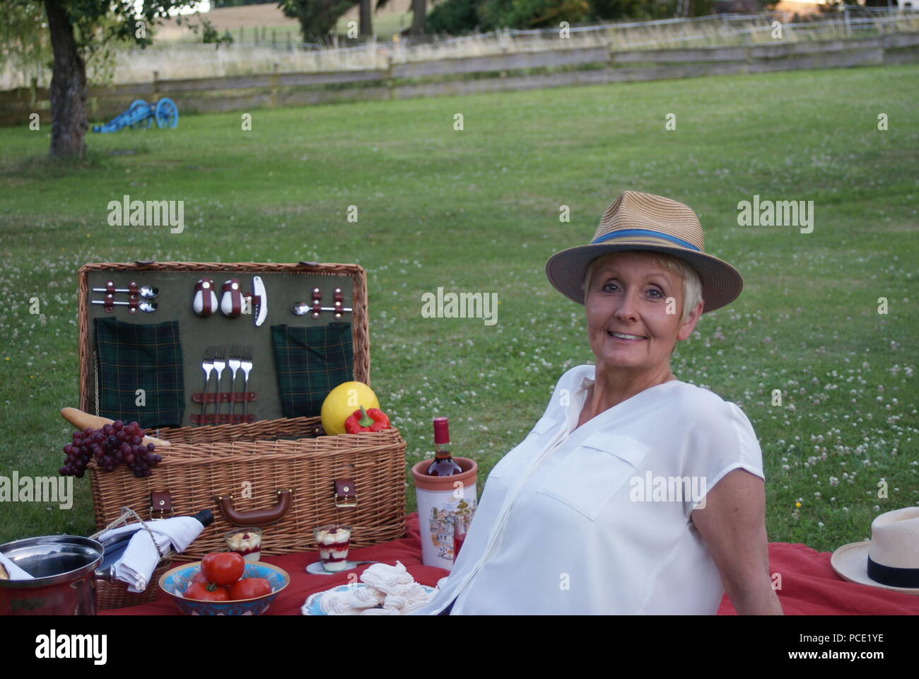 Rilassati con un cappello per il sole sulla sua testa, la donna bionda sorride al picnic Foto Stock