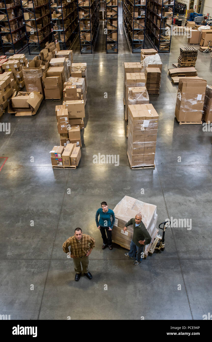 Un gruppo di tre magazzinieri in piedi al centro di un magazzino distirbution. Foto Stock