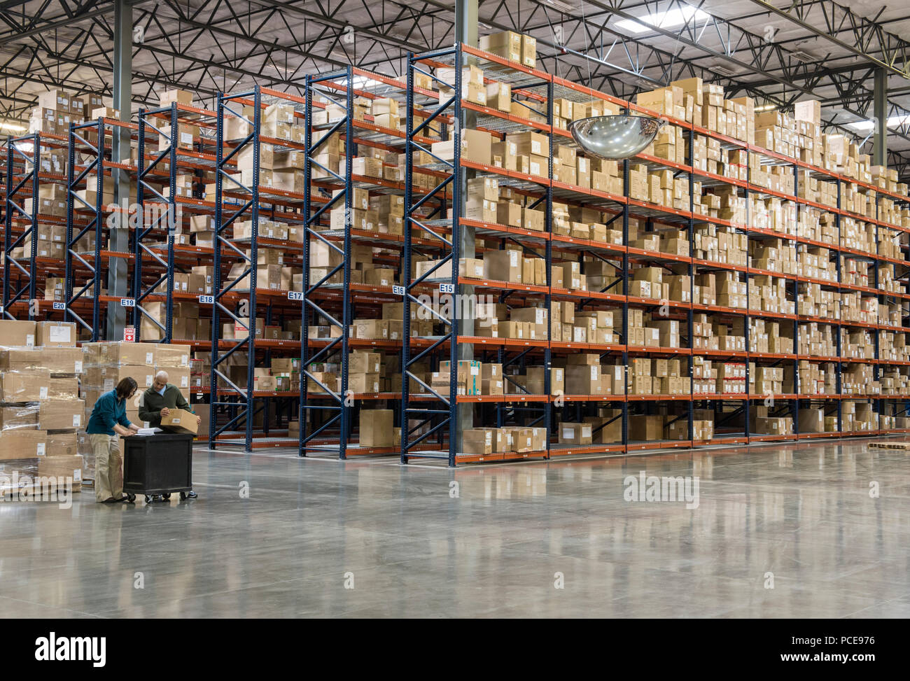 Due dipendenti di inventario di controllo accanto a cremagliere di scatole in deposito temporaneo in un magazzino di distribuzione. Foto Stock