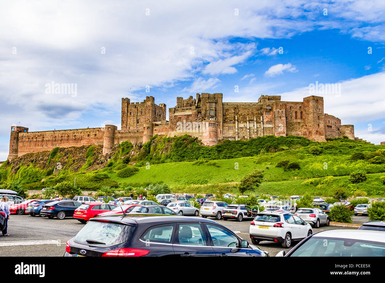 Occupato parcheggio auto sul bordo del piccolo villaggio di Bamburgh, rivolto verso il castello di Bamburgh, Northumberland, Regno Unito. Foto Stock