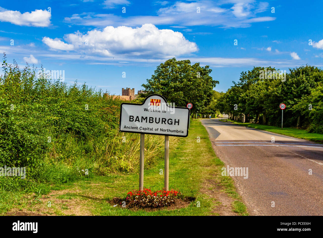 Segno accogliente gli automobilisti a Bamburgh village, con il castello di Bamburgh in background. Bamburgh, Northumberland, Regno Unito. Foto Stock