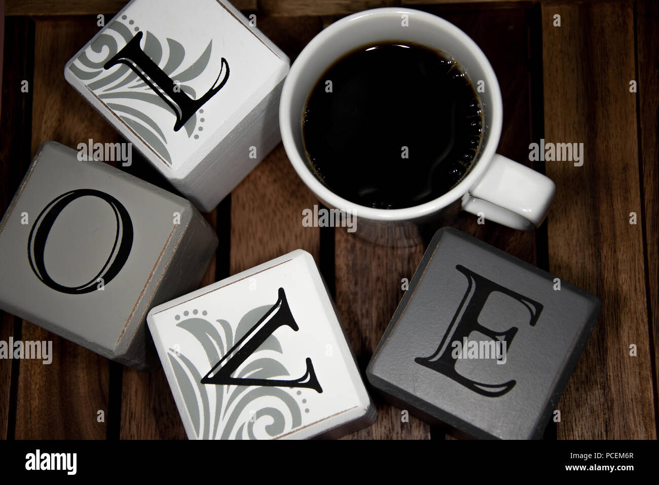 La parola amore con una tazza di caffè in un cerchio al buio su un sfondo di legno Foto Stock