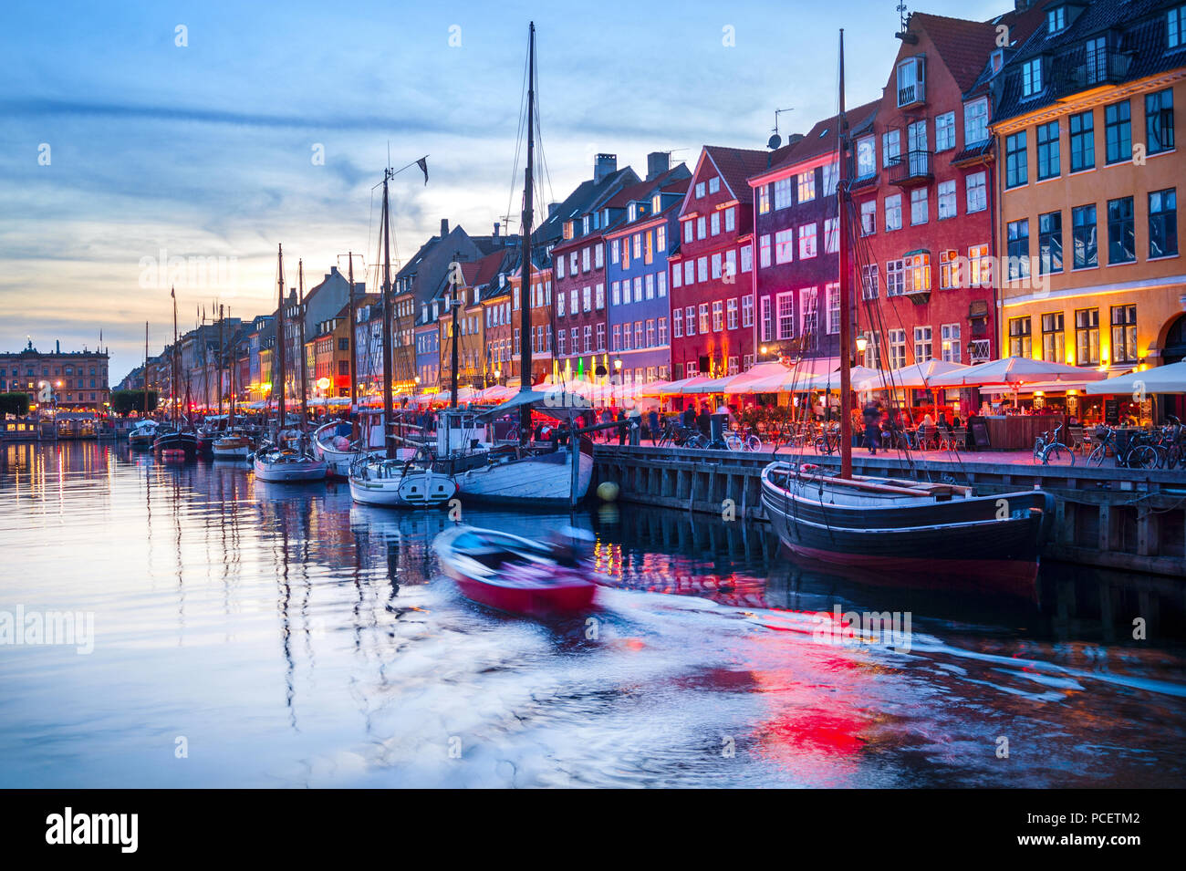 Scena serale con barche ormeggiate illuminato dal porto di Nyhavn embankment, Copenhagen, Danimarca Foto Stock