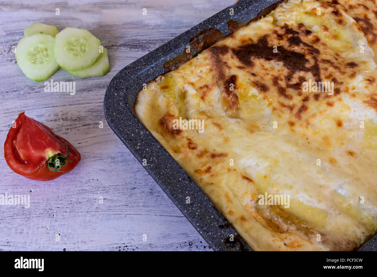 Il cibo italiano. Gustosi piatti caldi appena sfornati serviti di lasagne con pomodori e cetrioli su un tavolo di legno. Close-up, il fuoco selettivo. Foto Stock