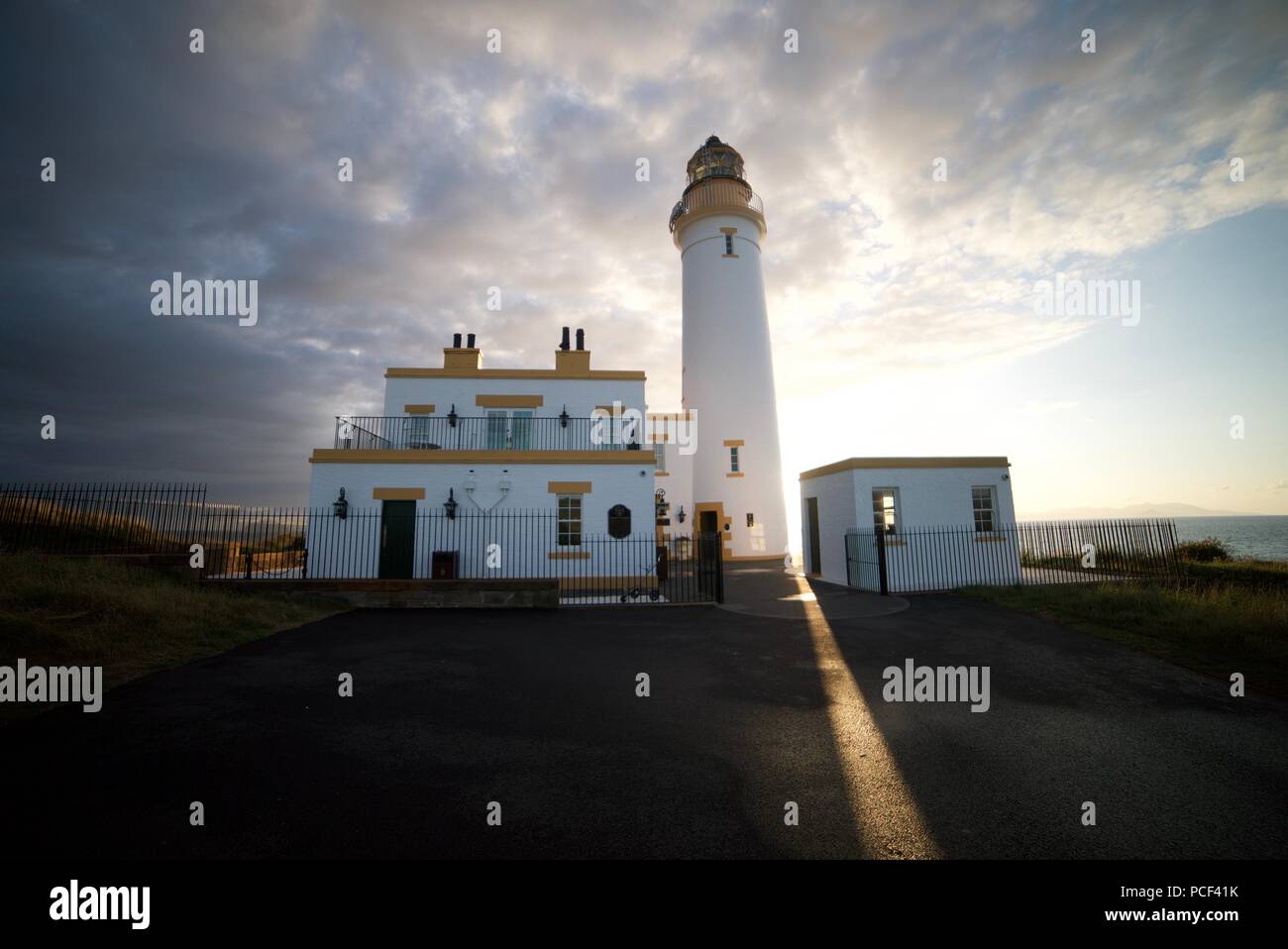 Il sole brilla dietro Turnberry faro presso la costa dell'Ayrshire accanto al Trump Turnberry Golf, al tramonto, con un cielo blu chiaro. Foto Stock
