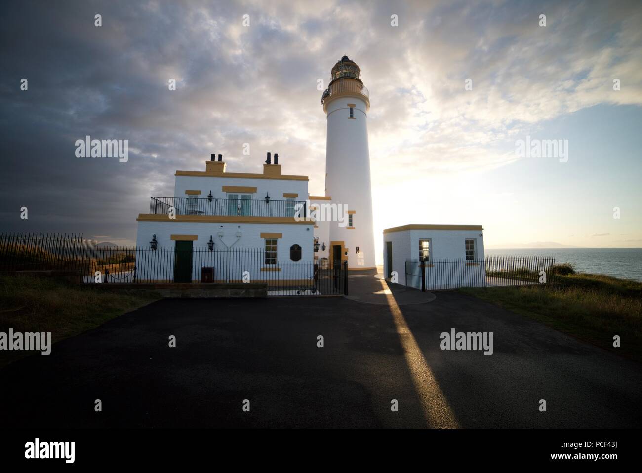 Il sole brilla dietro Turnberry faro presso la costa dell'Ayrshire accanto al Trump Turnberry Golf, al tramonto, con un cielo blu chiaro. Foto Stock