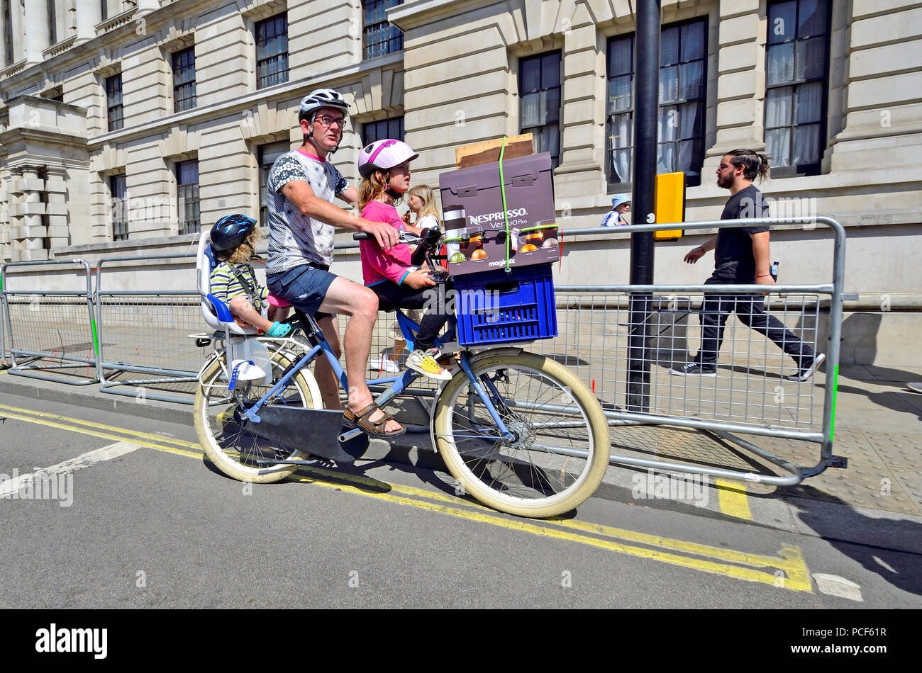 Padre con le sue due giovani figlie su una bicicletta, con un po' di shopping sulla parte anteriore, Whitehall, Londra, Inghilterra, Regno Unito. Foto Stock
