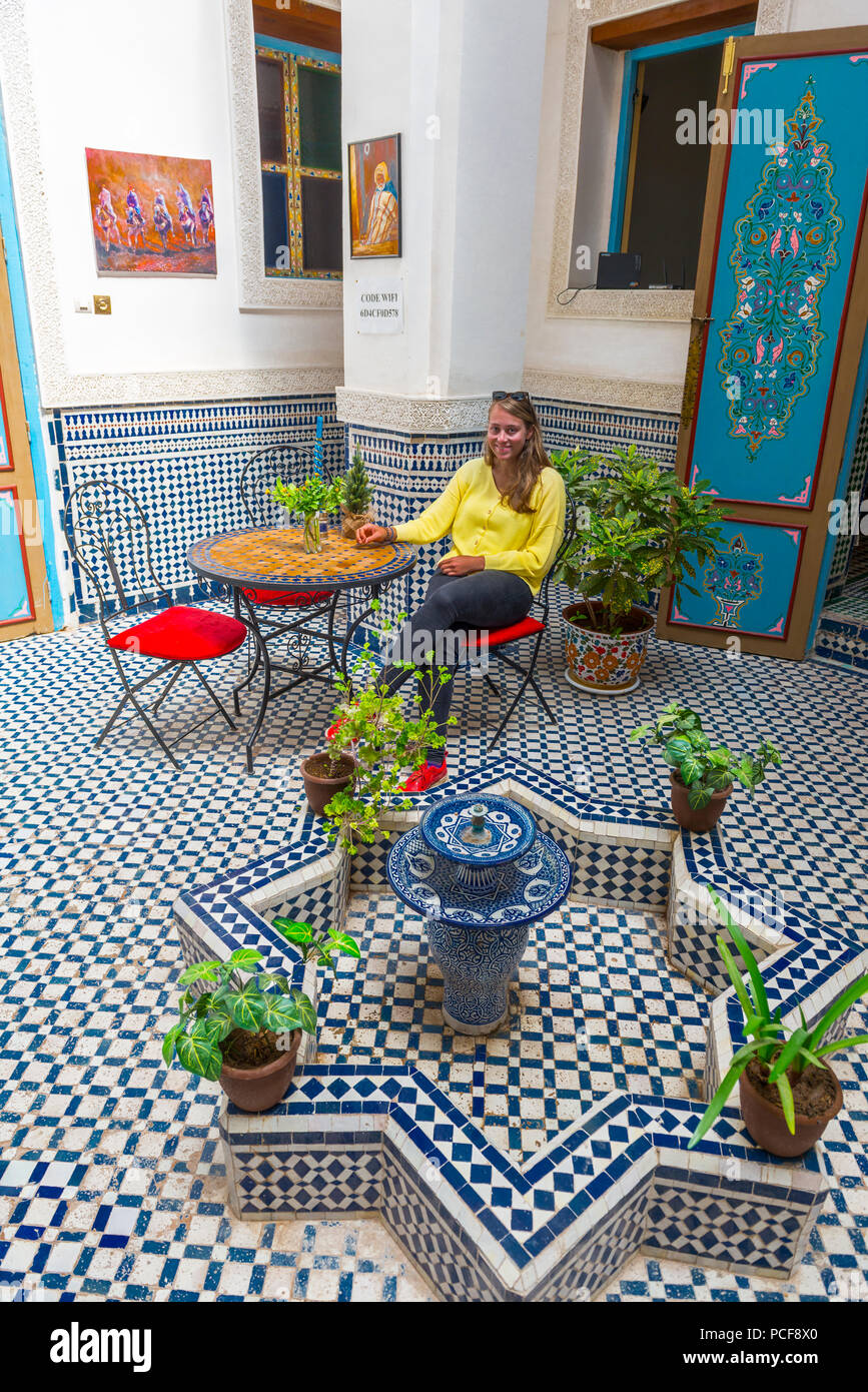 Giovane donna in un cortile marocchino, piastrelle blu e fontana, Fès-Boulemane, Marocco Foto Stock