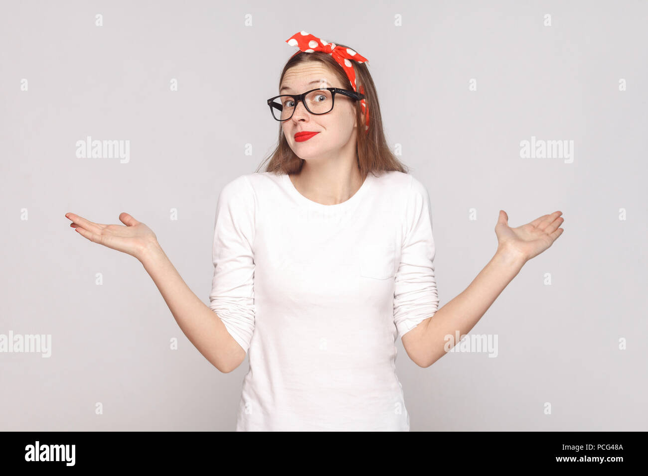 Non lo so. Non ho idea. ritratto della bella emotivo giovane donna in t-shirt bianca con lentiggini, occhiali neri, labbra rosse e head band. interna Foto Stock