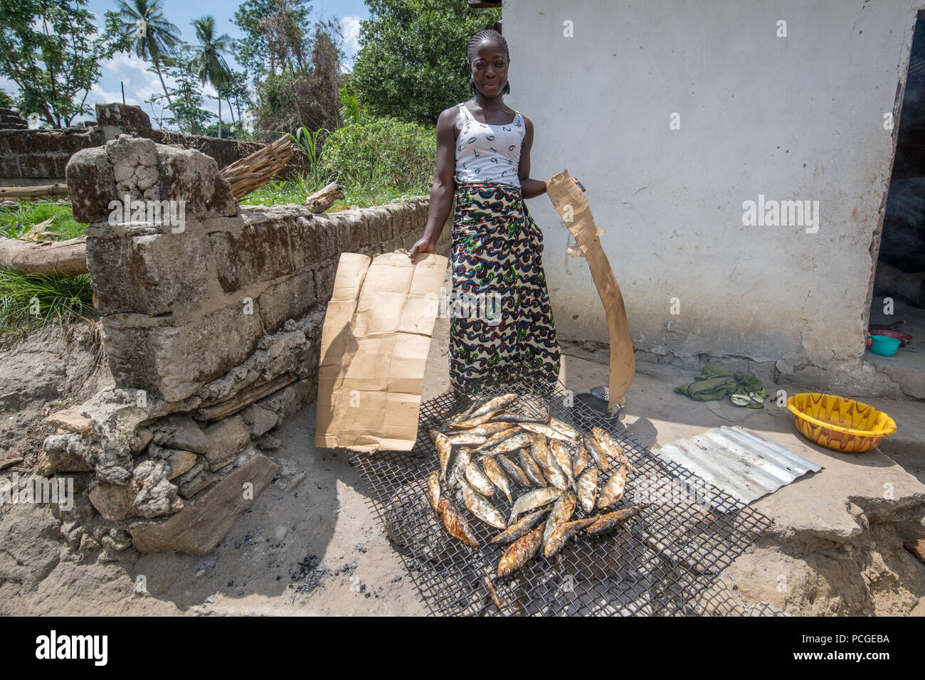 Una donna fuma pesce e pone per la fotocamera in Ganta, Liberia Foto Stock