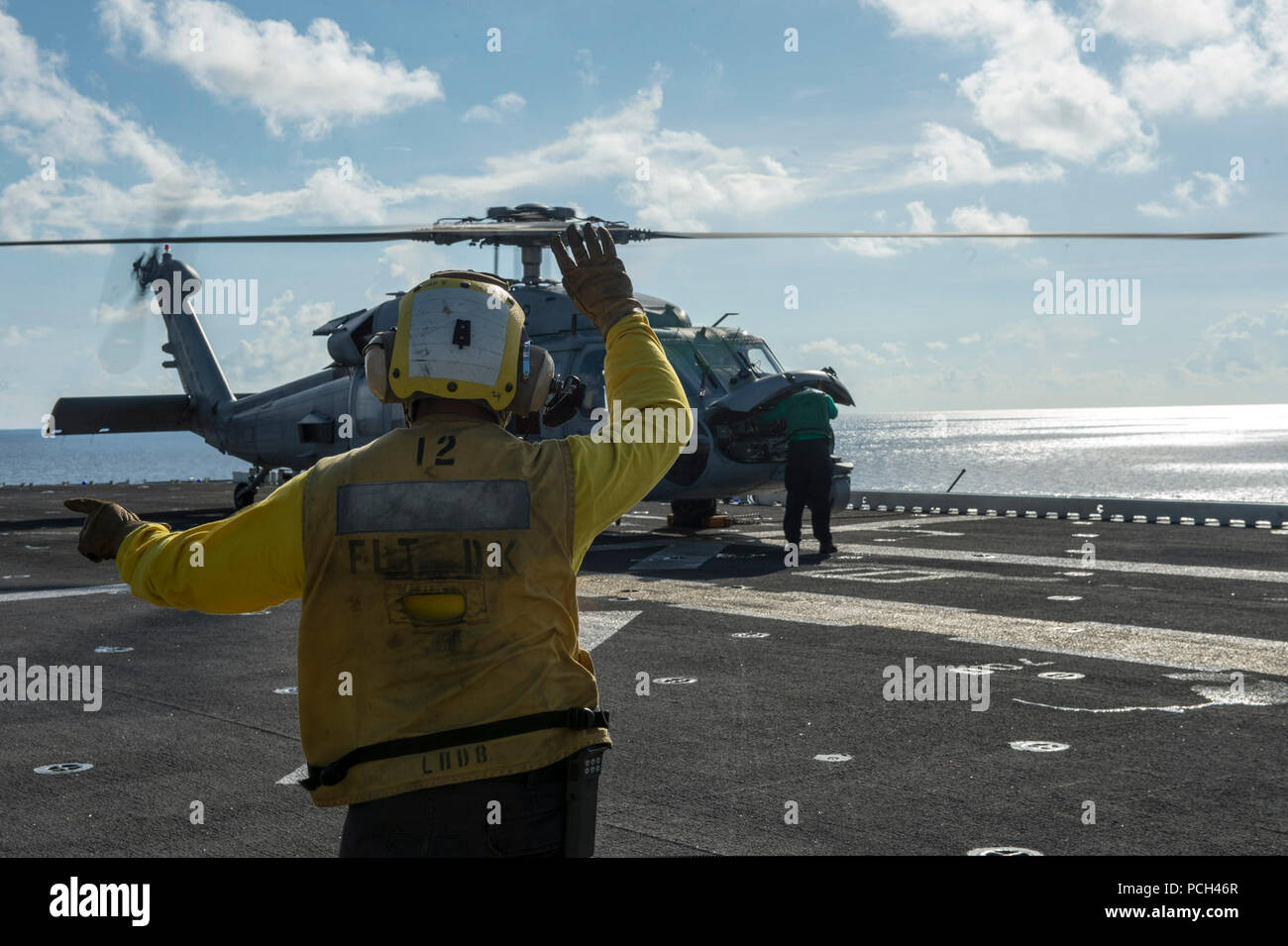 Un U.S. Sailor segnali per i piloti di un MH-60S Seahawk elicottero assegnato al mare in elicottero Combat Squadron (HSC) 23 sul ponte di volo dell'assalto anfibio nave USS Makin Island (LHD 8) nell'Oceano Pacifico il Agosto 25, 2014. La Makin Island era già in corso negli Stati Uniti 7 flotta area di responsabilità sostenere le operazioni di sicurezza marittima e di protezione del teatro gli sforzi di cooperazione. Foto Stock