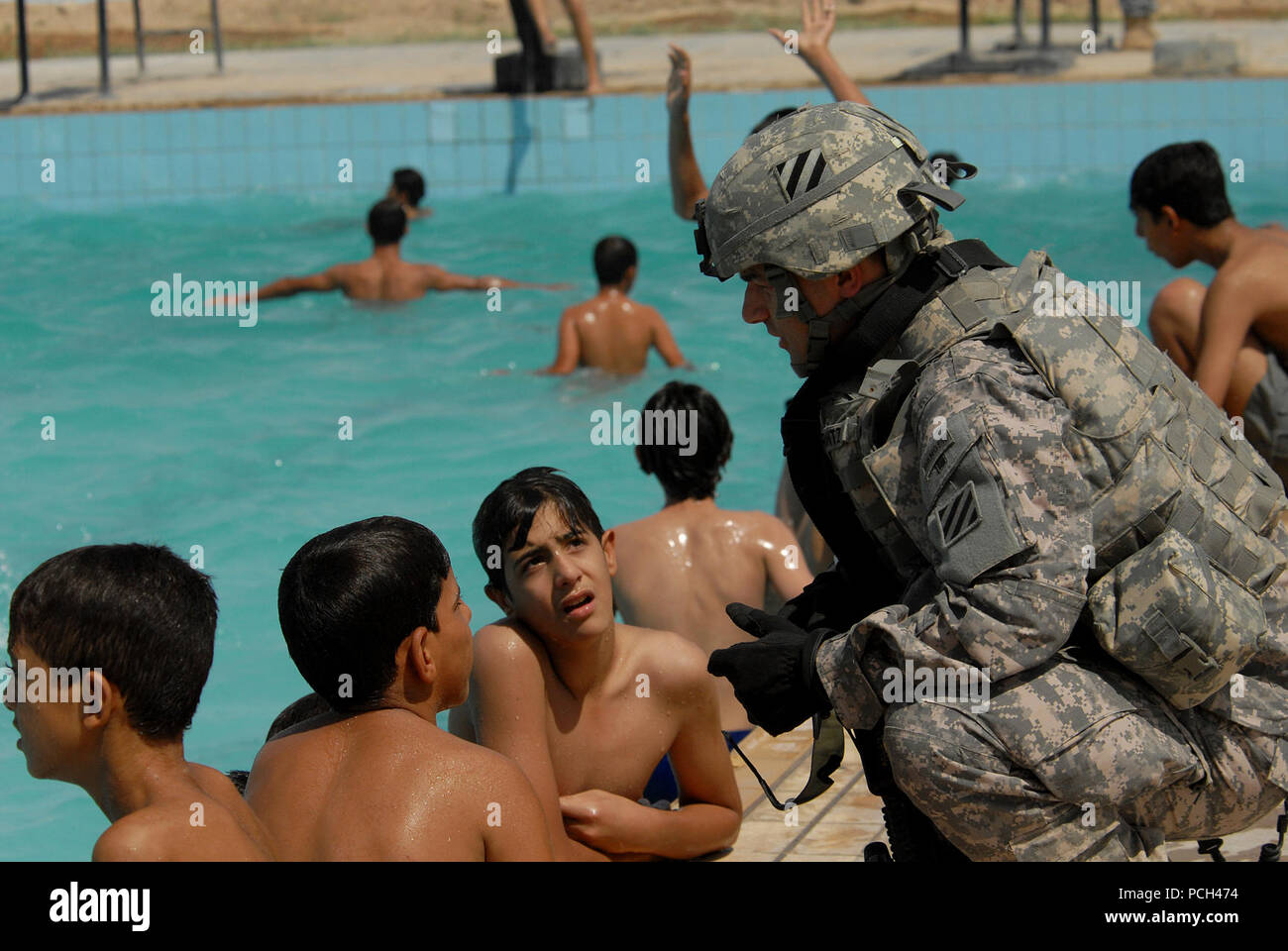 Un U.S. Soldato assegnato per la sicurezza personale di distacco, 4° Battaglione, 64th Armor reggimento, terza divisione di fanteria, parla agli iracheni boys come egli fornisce la sicurezza all'apertura di una nuova piscina in Risalah, Baghdad, Iraq, Sett. 18, 2008. Foto Stock