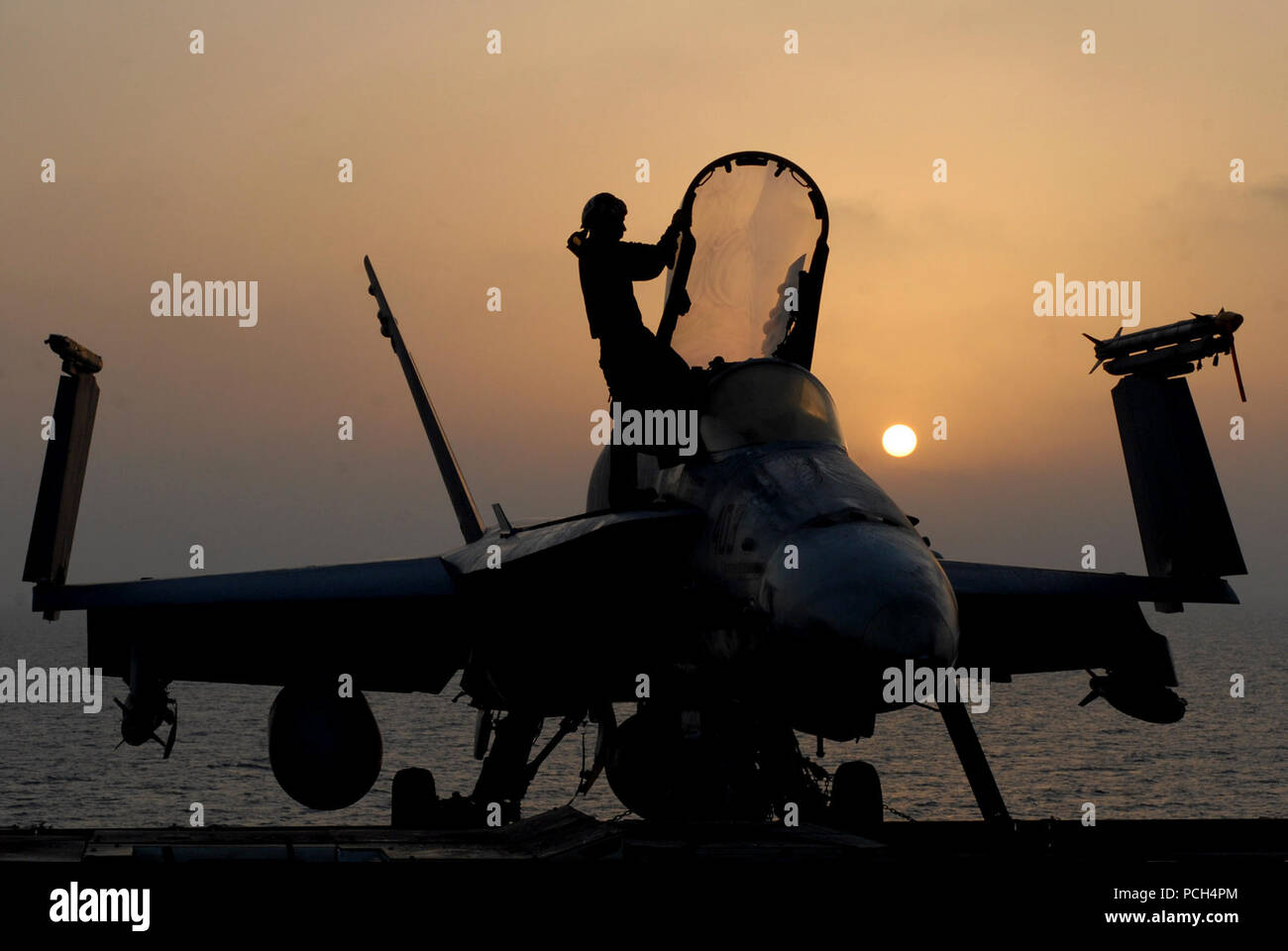 Un F/A-18C Hornet assegnato al "pugno di Flotta" di Strike Fighter Squadron 25 siede parzialmente stagliano contro il cielo arancione di un Rising Sun come Sottufficiali di terza classe Kyle Alhers esegue la sua routine mattutina. La routine per un piano capitano inizia molto prima che il sole sorge e molte volte si possono eseguire fino a tarda notte. La Nimitz-class portaerei USS Ronald Reagan è attualmente implementata per la Quinta Flotta/NAVCENT area di responsabilità. Le operazioni in NAVCENT area di operazioni sono incentrate sulla rassicurante partner regionale dell'impegno degli Stati Uniti per la sicurezza che promo Foto Stock