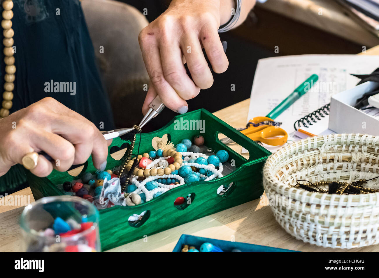 Mani femminili servendosi di una pinza per fare un bracciale utilizzando metallo e accessori in plastica a lavorare presso la sua officina. Foto Stock