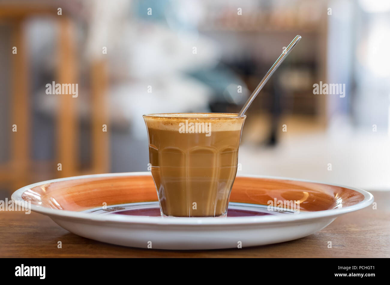 Un caffè caldo con il latte su un vetro trasparente con un cucchiaio collocato al disopra di una piastra, closeup. Foto Stock