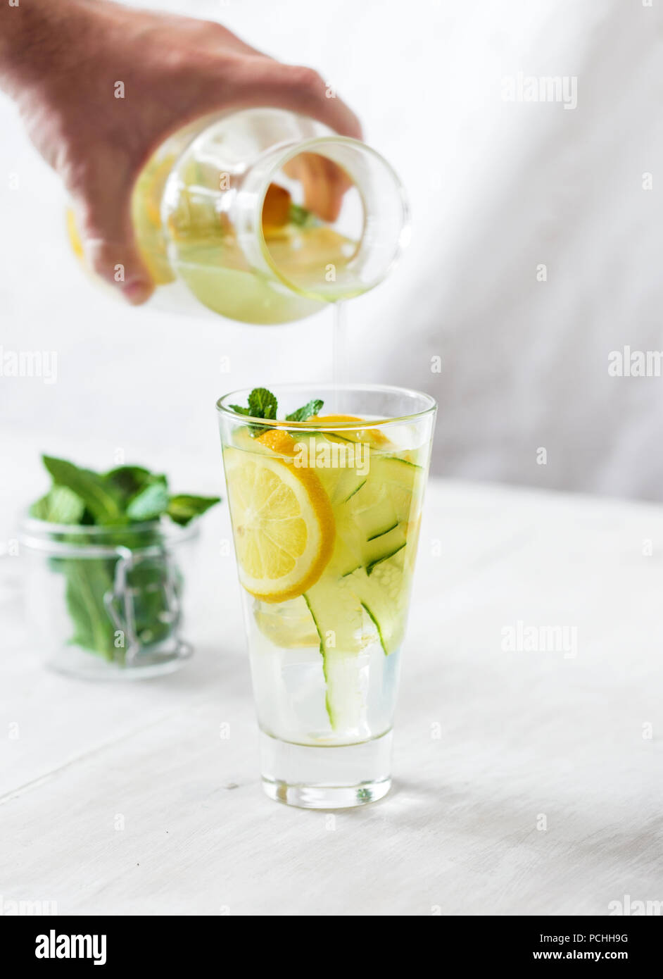L uomo si riversa nel bicchiere detox acqua con il cetriolo, limone e menta Foto Stock