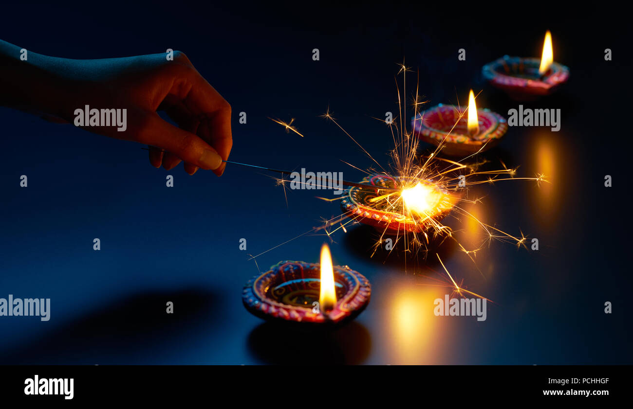 Felice Diwali - Illuminazione un sparkler con lampada diya Foto Stock