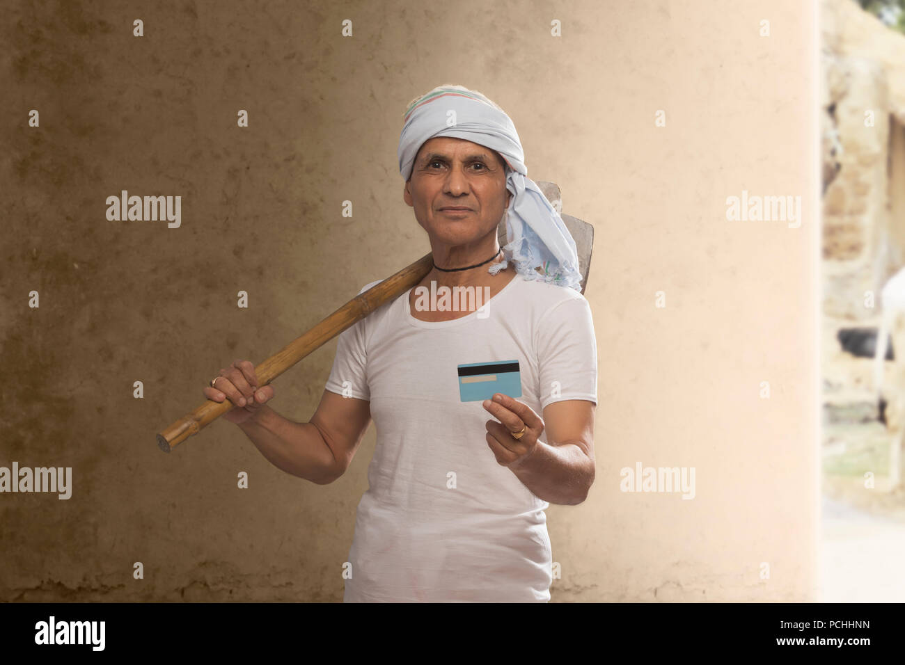 Ritratto di Indian vecchio contadino tenendo la carta di credito e portando la zappa sulla spalla Foto Stock