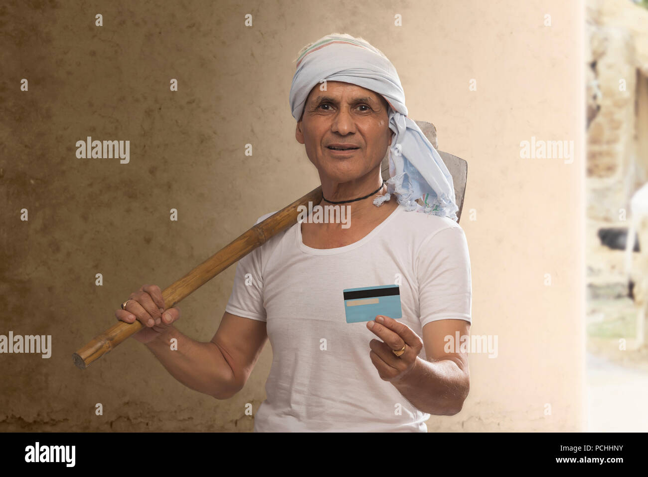 Ritratto di Indian vecchio contadino tenendo la carta di credito e portando la zappa sulla spalla Foto Stock