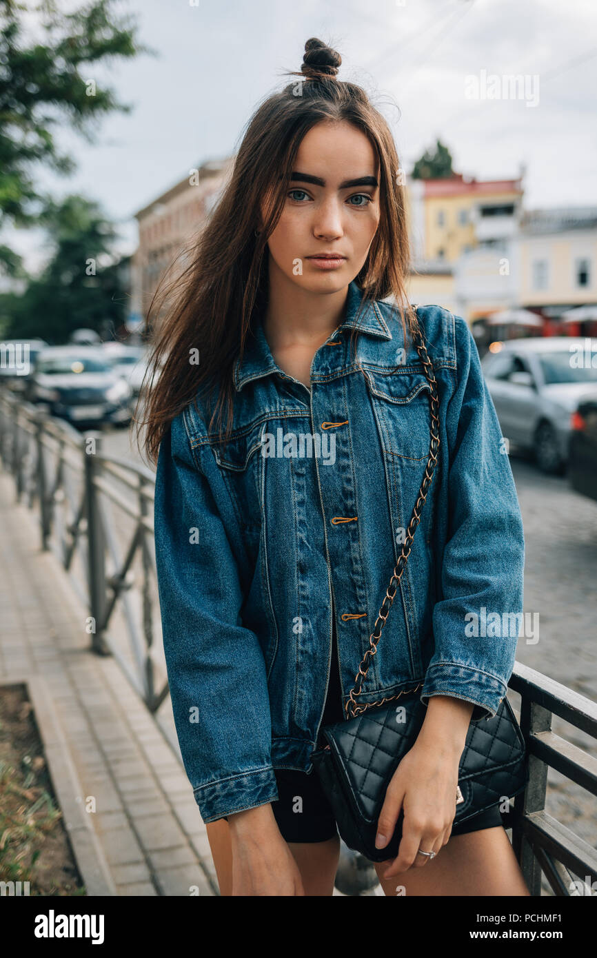 Giovane donna con capelli lunghi vestiti in camicia denim permanente sulla  strada vicino alla strada. Carino elegante ragazza teen in posa nella città  Foto stock - Alamy