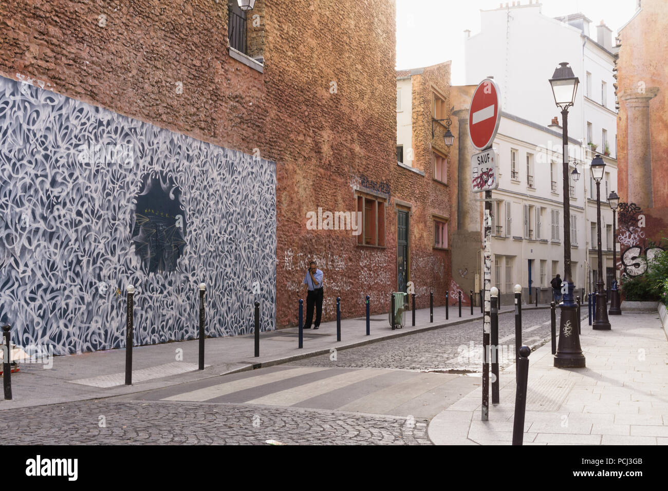 Paris Street scene - angolo di rue Legouve e Rue Lucien Sampaix, un uomo parla al telefono accanto alla strada murale. In Francia, in Europa. Foto Stock