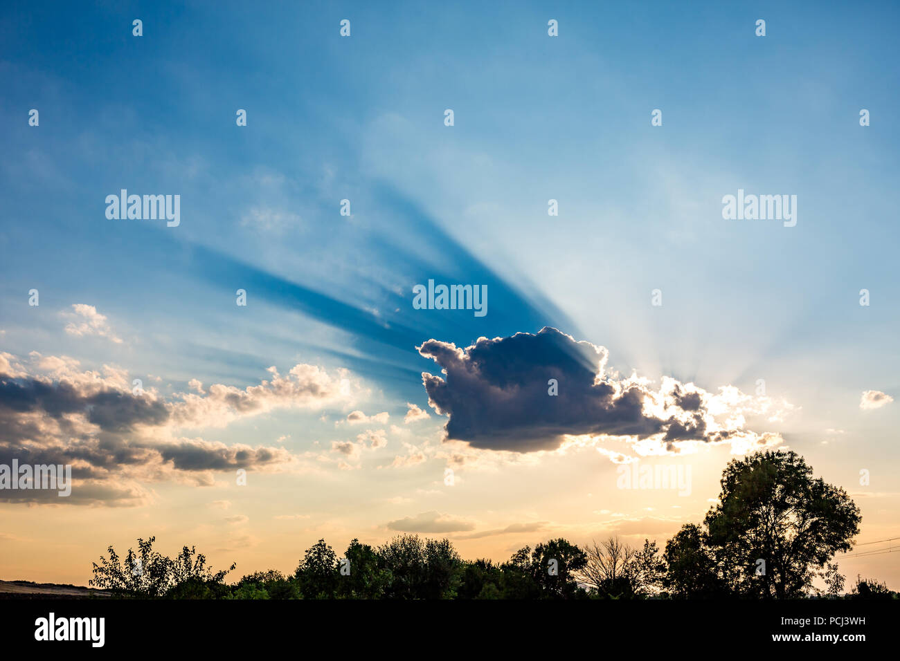 Colorato tramonto cielo con le nuvole e il sole sembra scoppiare fuori da dietro di loro gettando bella blu cast. Alcuni alberi nella parte anteriore. Bulgari Foto Stock