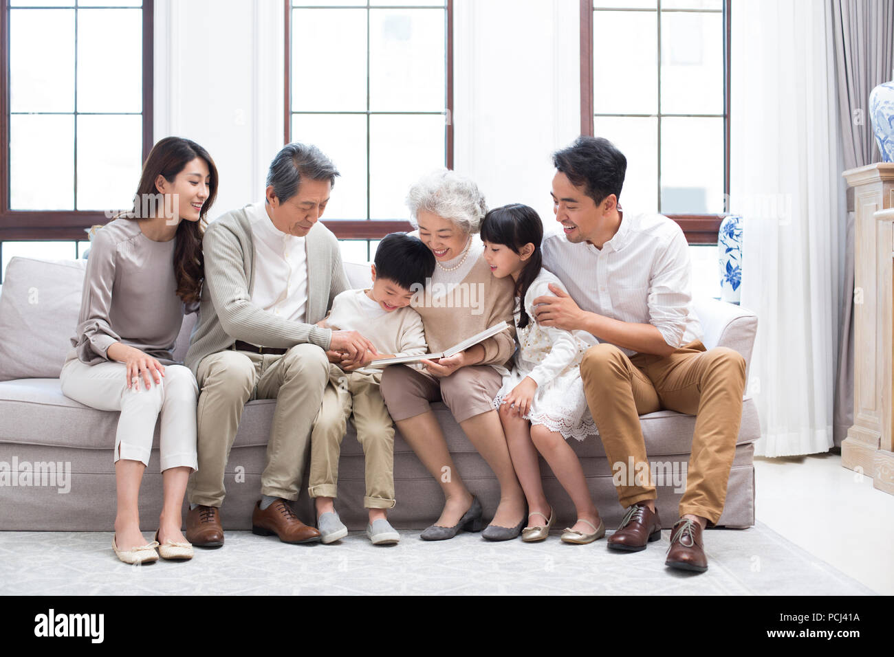 Felice famiglia cinese guardando album di foto sul divano Foto Stock