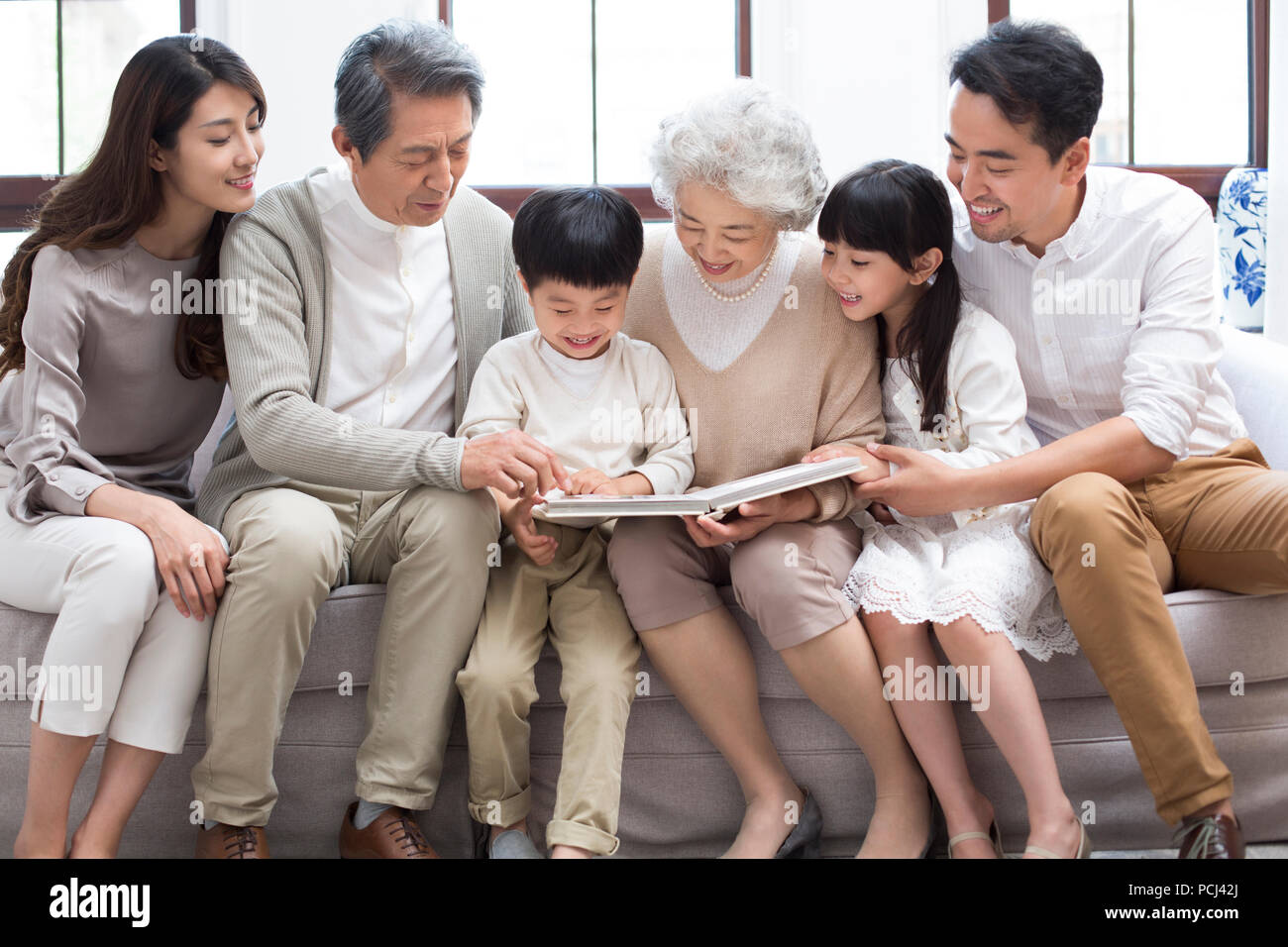 Felice famiglia cinese guardando album di foto sul divano Foto Stock