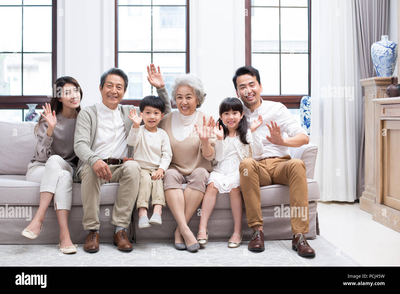 Felice famiglia cinese sventolare sul divano Foto Stock