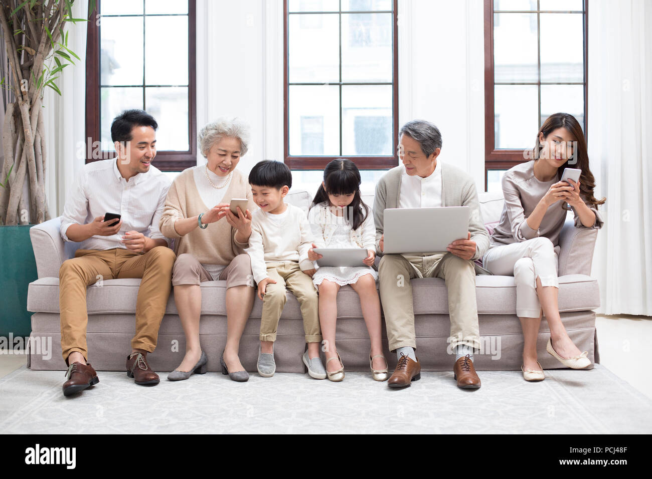 Felice famiglia cinese utilizzando dispositivi digitali sul divano Foto Stock