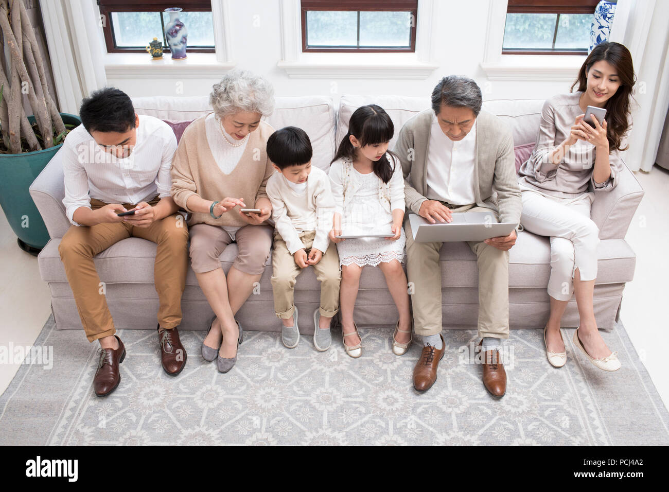 Felice famiglia cinese utilizzando dispositivi digitali sul divano Foto Stock